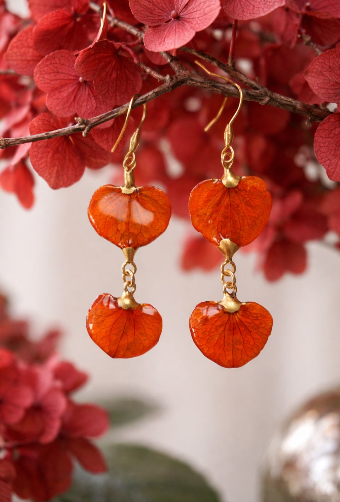 Dettaglio orecchini doppi con petali di ortensia arancio in resina e montatura dorata